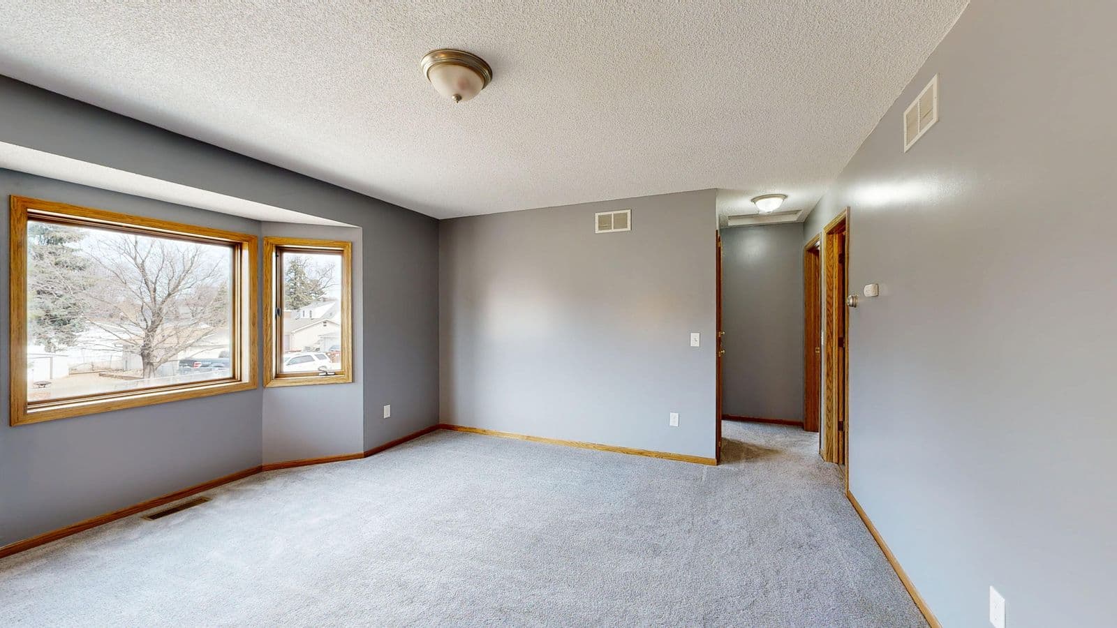 Bright, empty room with grey carpet flooring and large windows
